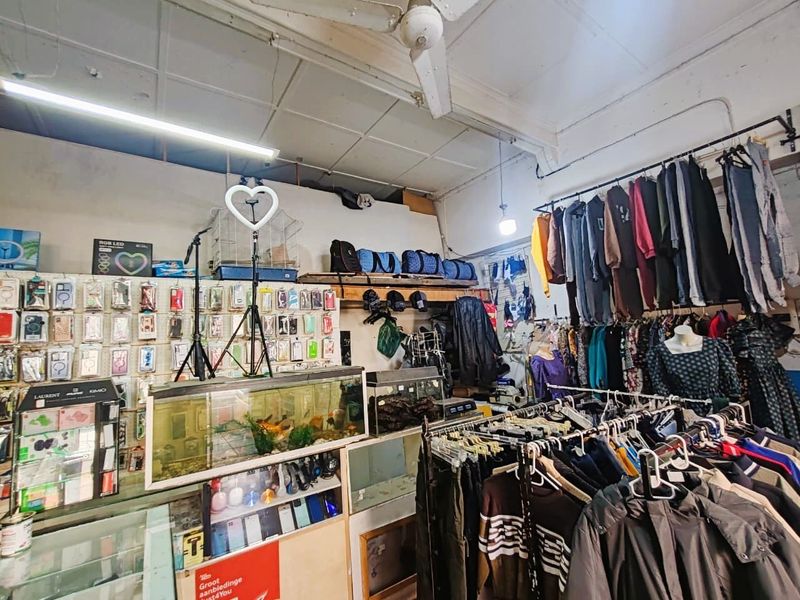 Retail space featuring ceiling-mounted lighting, wall-mounted clothing rails, and built-in display shelving, currently utilized for apparel and accessory sales.