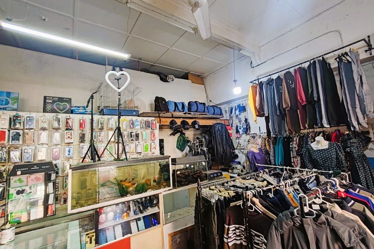 Retail space featuring ceiling-mounted lighting, wall-mounted clothing rails, and built-in display shelving, currently utilized for apparel and accessory sales.