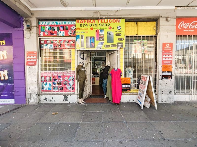Front elevation of a retail shop unit featuring security gates, metal window bars, and prominent commercial signage on a paved street-level frontage.