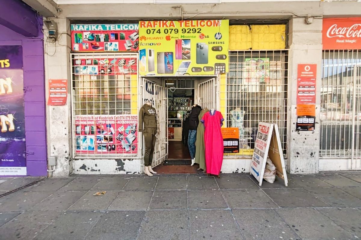Front elevation of a retail shop unit featuring security gates, metal window bars, and prominent commercial signage on a paved street-level frontage.