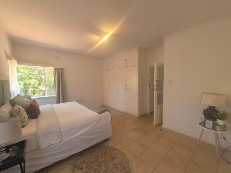A spacious bedroom featuring built-in cupboards, neutral tiled flooring, and a large window allowing for natural light.