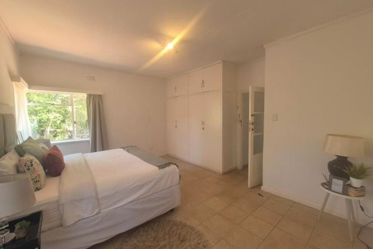 A spacious bedroom featuring built-in cupboards, neutral tiled flooring, and a large window allowing for natural light.