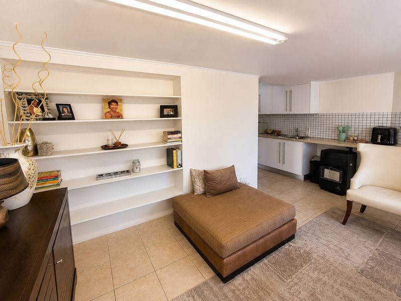 Open plan living area featuring tiled flooring, built-in shelving, and a functional kitchen with white cabinetry and tiled backsplash.