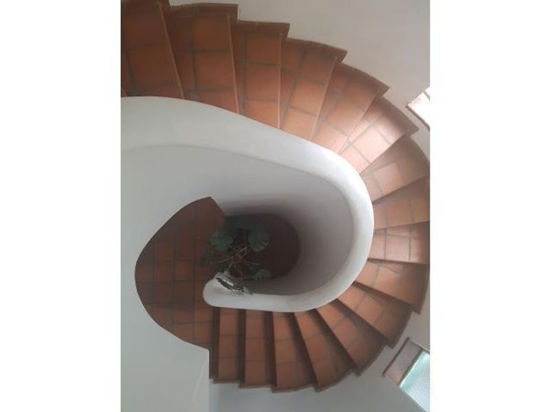 A top-down view of a spiral staircase featuring terracotta tiled steps and a solid white plaster balustrade.