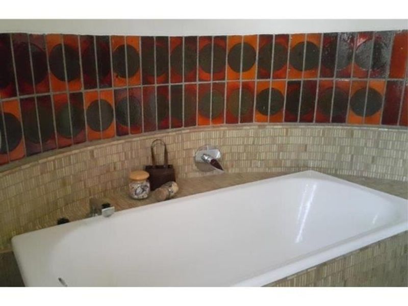 A bathroom featuring a built-in bathtub with a chrome mixer tap and a distinctive retro-style mosaic and patterned tile splashback.