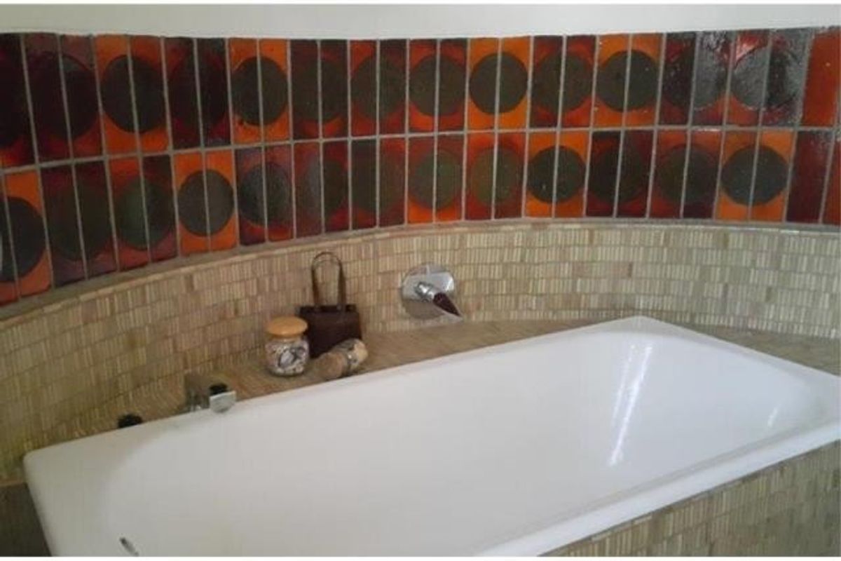 A bathroom featuring a built-in bathtub with a chrome mixer tap and a distinctive retro-style mosaic and patterned tile splashback.
