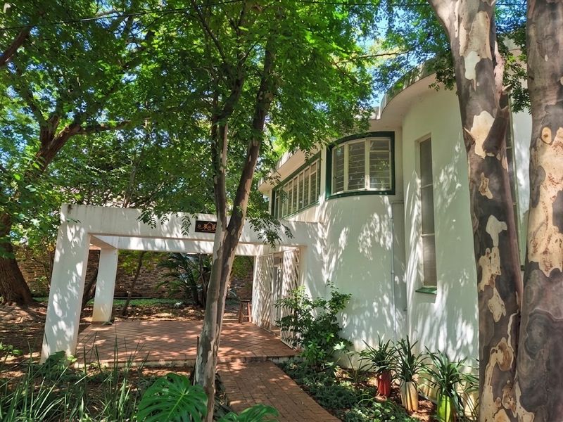 A view of the rear exterior featuring a covered patio area, curved architectural wall, and established garden surroundings.