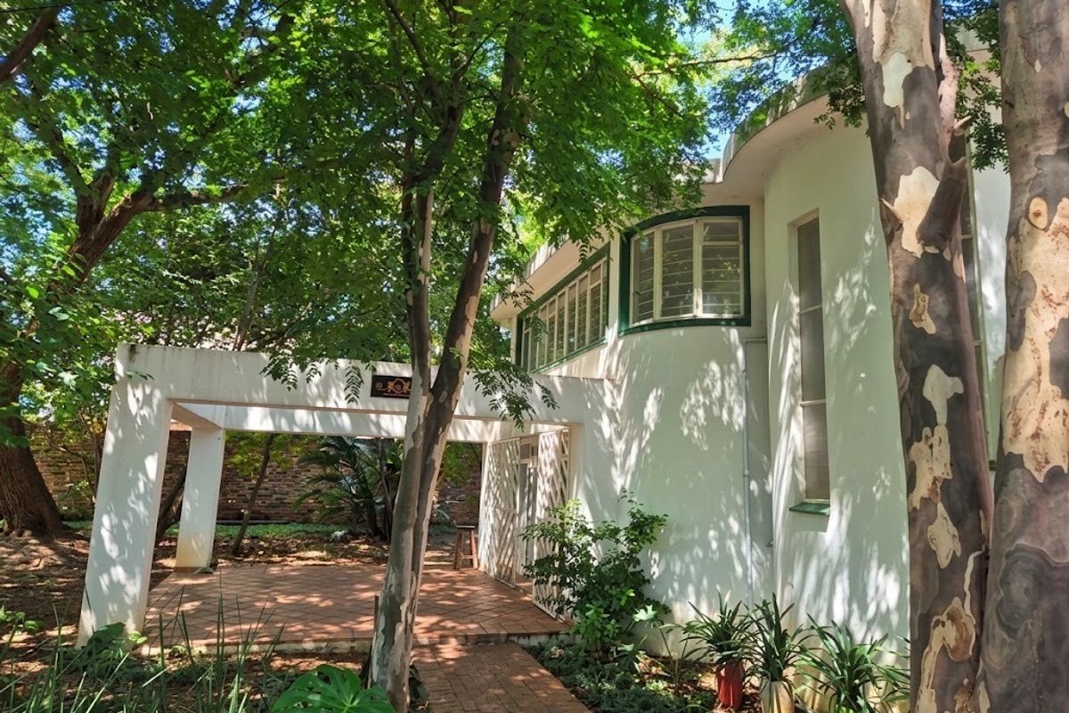 A view of the rear exterior featuring a covered patio area, curved architectural wall, and established garden surroundings.