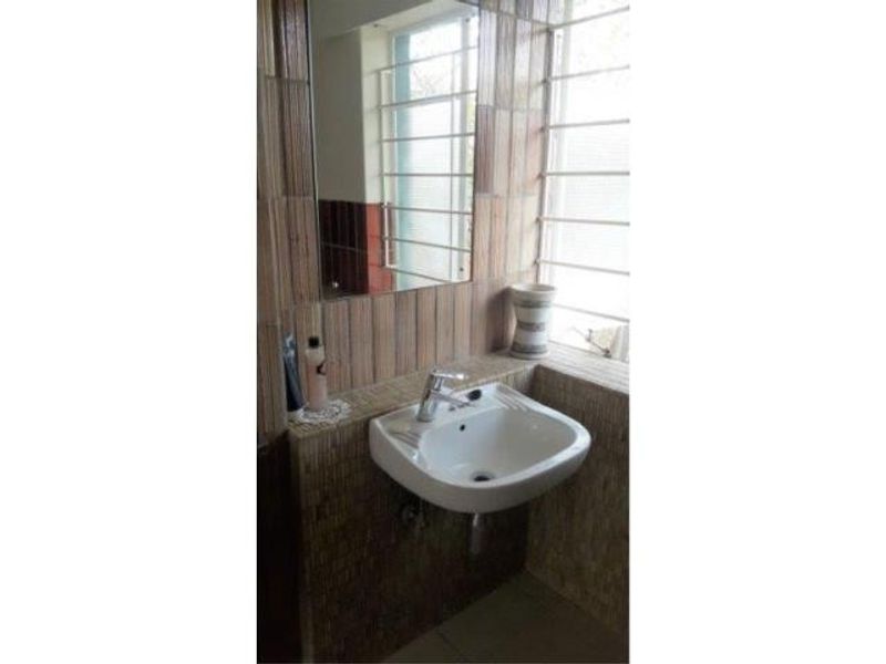 A compact bathroom featuring a wall-mounted basin with a chrome mixer tap, tiled wall finishes, and a large mirror.