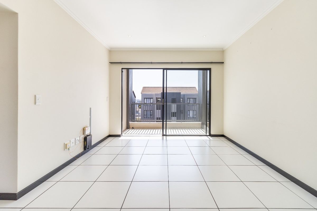 A bright, empty living room featuring white tiled flooring, recessed lighting, and a sliding glass door leading to a private balcony.