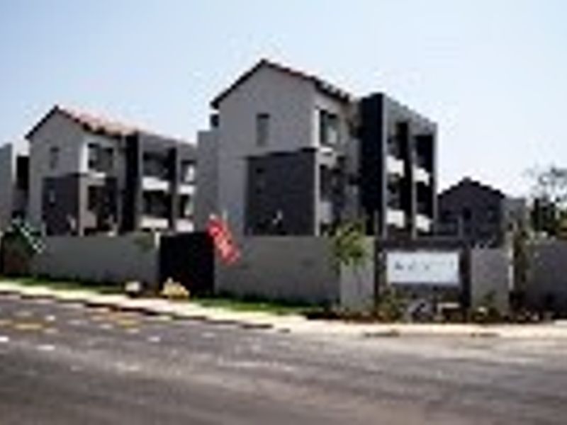 Street view of a modern apartment complex featuring multi-story residential blocks, secure perimeter walling, and a gated entrance.