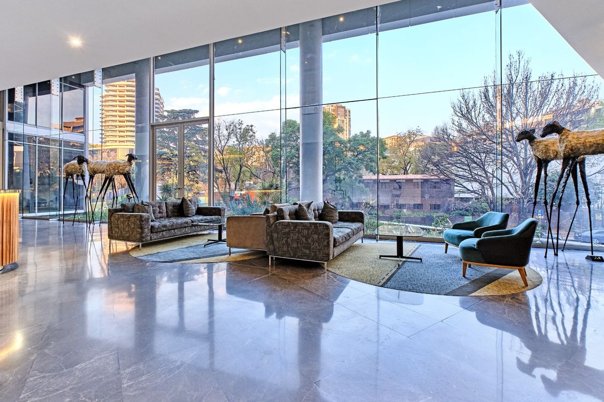 Spacious modern living area featuring expansive floor-to-ceiling glass windows, polished marble floors, and structural columns with views of the surrounding urban landscape.