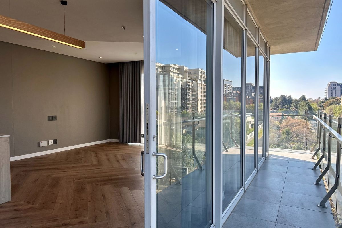 Modern open-plan living area featuring herringbone timber flooring, floor-to-ceiling glass doors, and a spacious balcony with glass balustrades offering urban views.