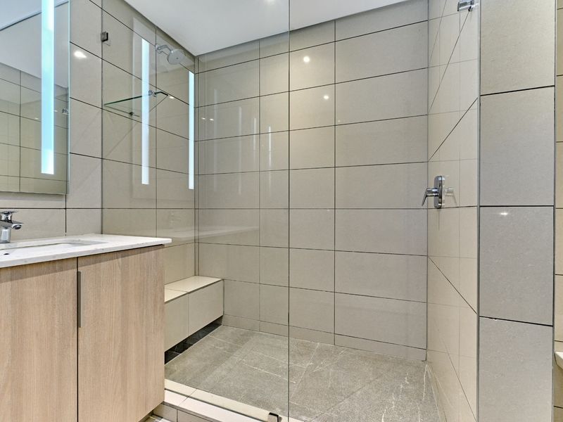 Modern bathroom featuring a spacious walk-in shower with glass screen, stone-topped vanity, wall-hung toilet, and contemporary tiled finishes.