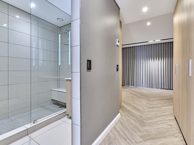 Modern bathroom featuring a glass-enclosed shower with a built-in bench, adjacent to a hallway with herringbone flooring and integrated cabinetry.