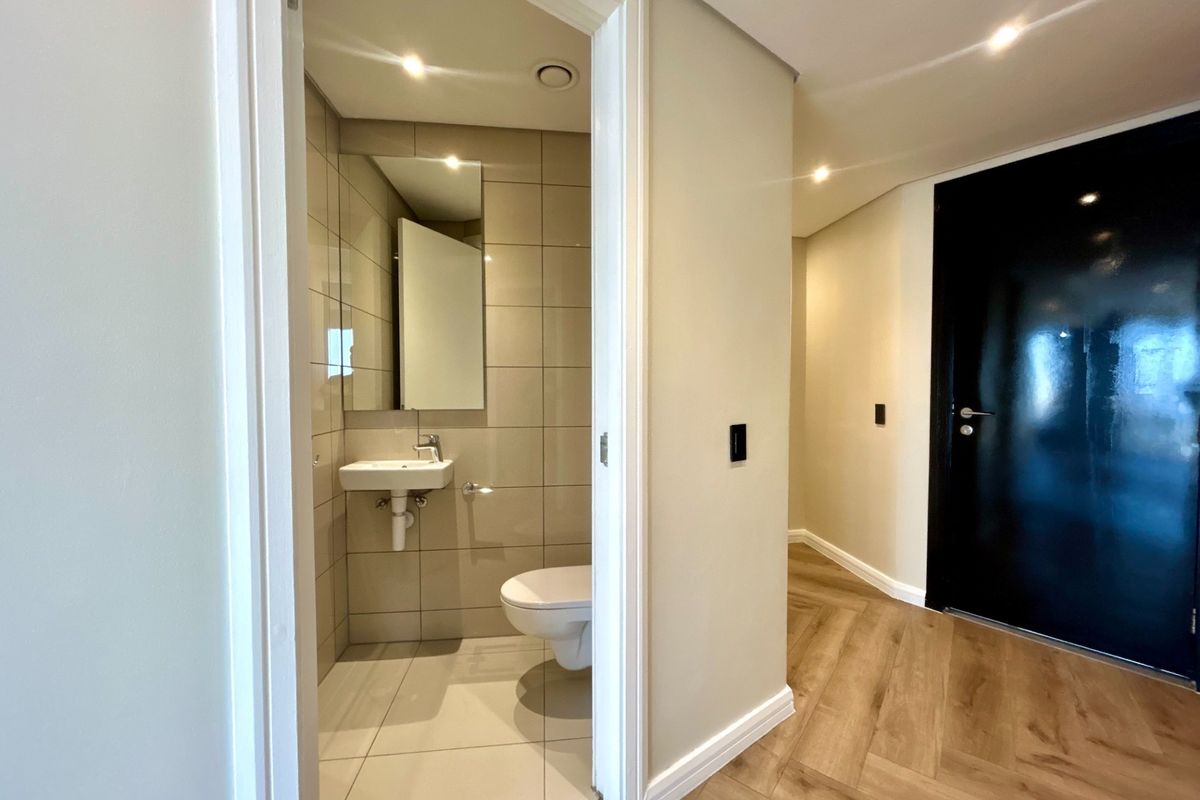 A modern guest bathroom featuring a wall-mounted toilet and basin, complemented by neutral wall tiles and adjacent wood-look laminate flooring in the hallway.