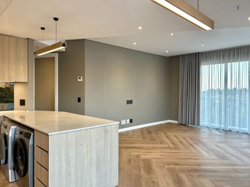 Modern open-plan living area featuring herringbone timber flooring, a sleek kitchen island with stone countertop, and floor-to-ceiling curtains leading to a balcony.