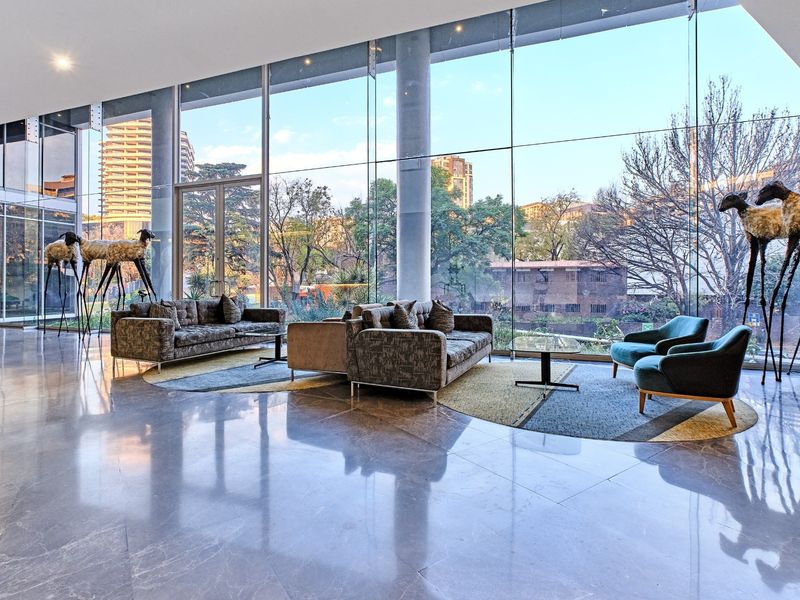 Spacious modern living area featuring expansive floor-to-ceiling glass windows, polished marble floors, and structural columns with views of the surrounding urban landscape.