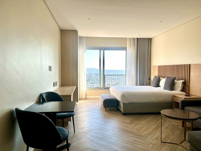 A modern, well-lit bedroom featuring herringbone flooring, a custom slatted timber headboard, built-in cabinetry, and a sliding glass door with scenic views.