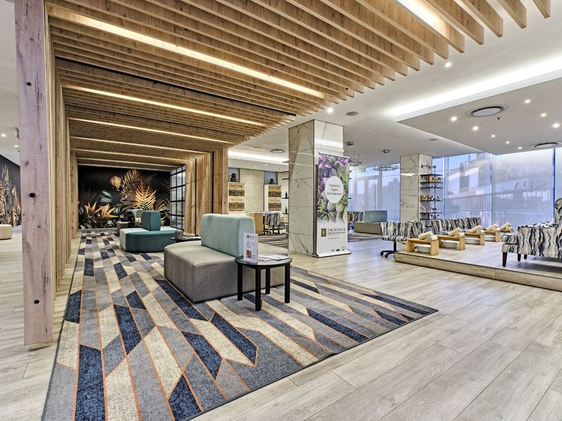 Modern clubhouse or spa reception area featuring a striking timber slat ceiling, marble column accents, and expansive glass windows providing natural light.