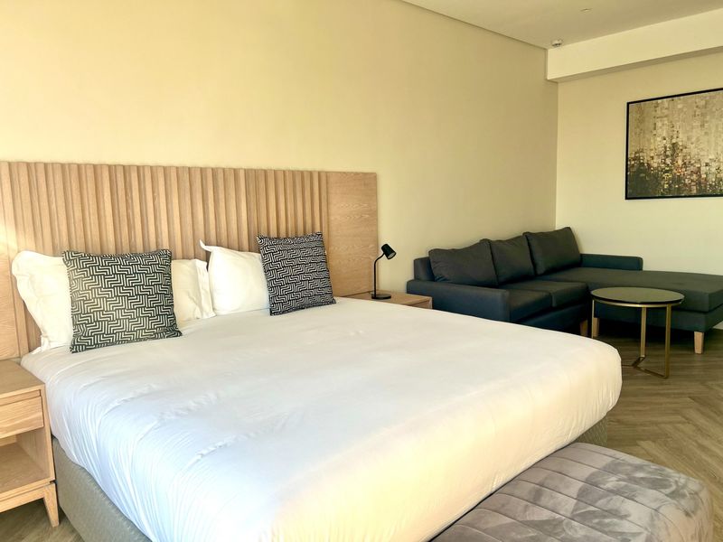 A well-maintained bedroom featuring a custom built-in headboard, recessed ceiling lighting, and modern herringbone flooring.