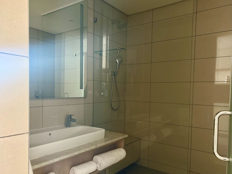 Modern bathroom featuring a vanity basin with mixer tap, wall-mounted mirror, and a glass-enclosed shower with tiled walls.