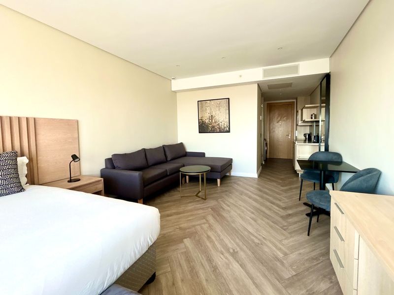 Modern open-plan studio apartment featuring herringbone flooring, recessed lighting, ducted air conditioning, and a compact kitchenette with timber cabinetry.