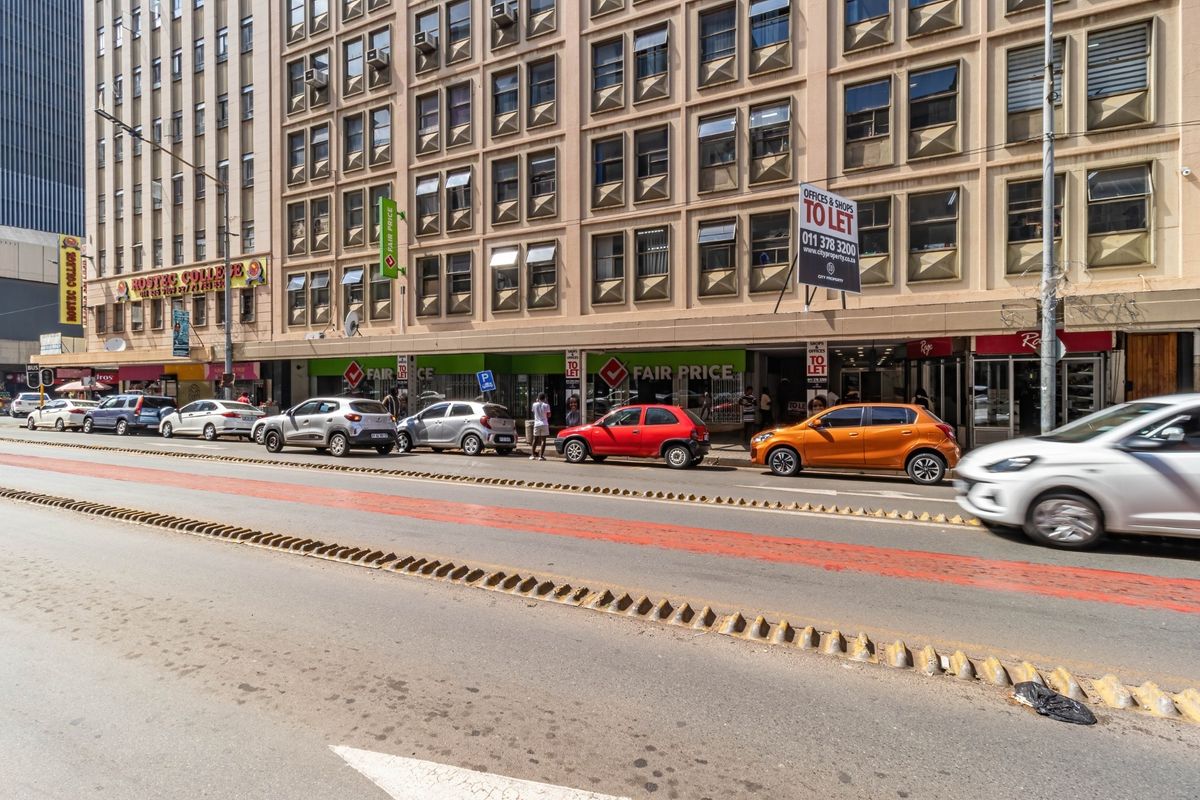 Street-level view of a multi-story commercial building featuring ground-floor retail storefronts and office space above in a busy urban setting.