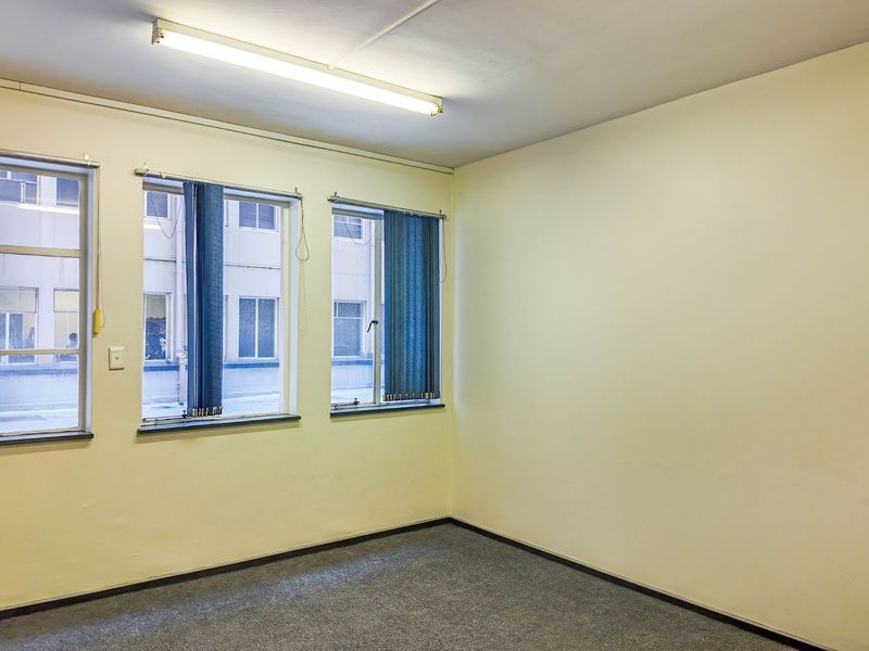 A vacant office space featuring neutral walls, carpet flooring, and large windows with vertical blinds, providing a functional blank canvas for commercial use.