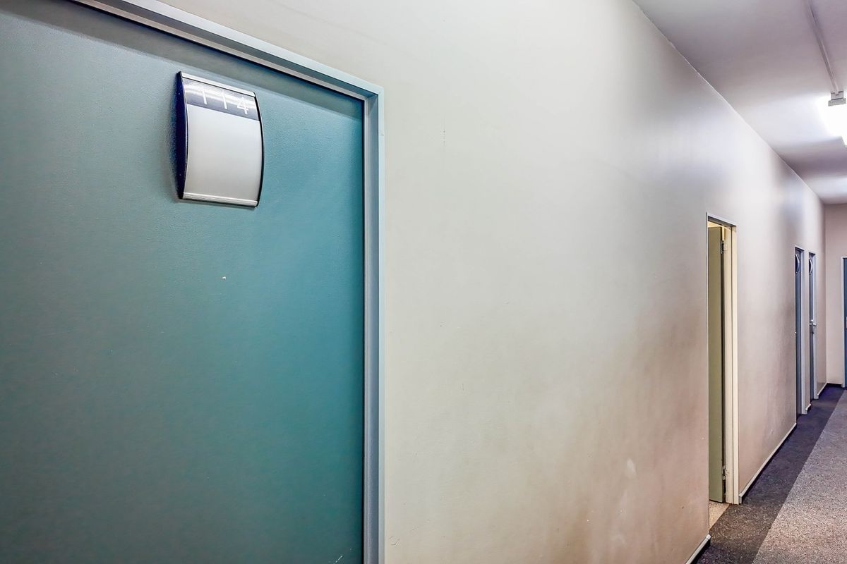 A commercial hallway featuring multiple doors with signage, fluorescent lighting, and carpeted flooring.