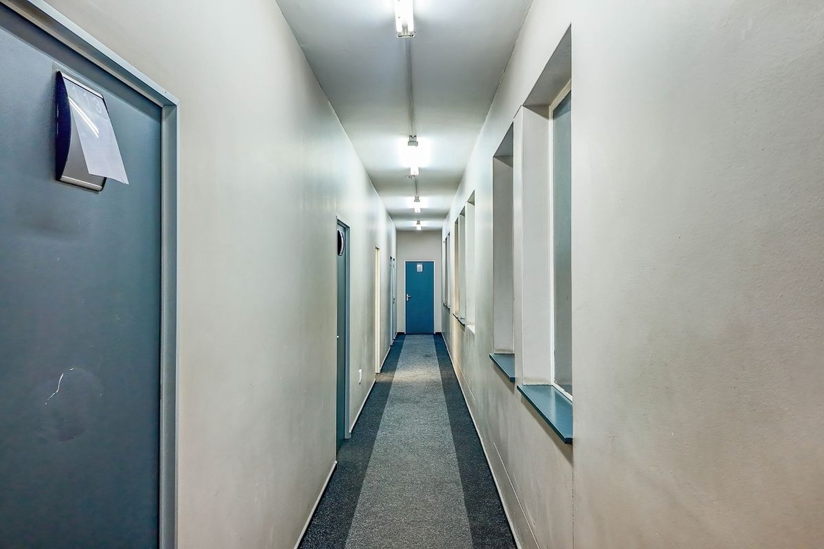 A functional commercial hallway featuring multiple internal access doors, fluorescent lighting, and carpeted flooring.