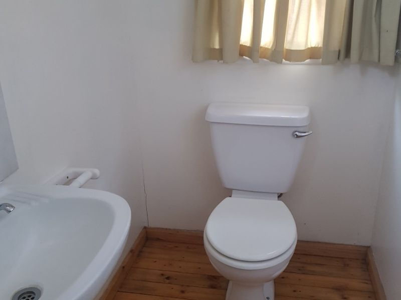 A compact bathroom featuring a pedestal basin, standard toilet, and timber flooring, requiring minor cosmetic updates to the wall finishes.