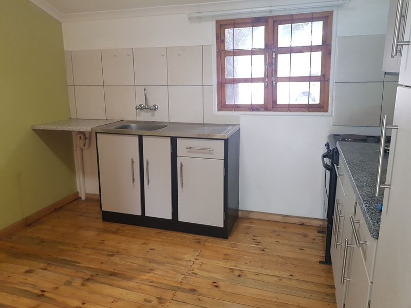 A functional kitchen area featuring timber flooring, built-in cabinetry, a stainless steel sink, and a freestanding stove with granite countertops.