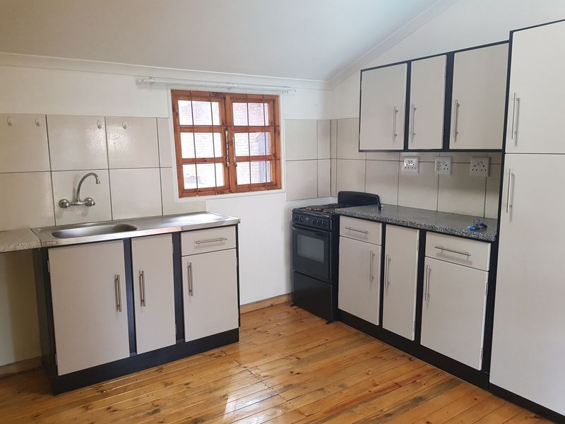 A functional kitchen featuring built-in cabinetry, a stainless steel sink, tiled splashback, and a freestanding stove, set against timber flooring.