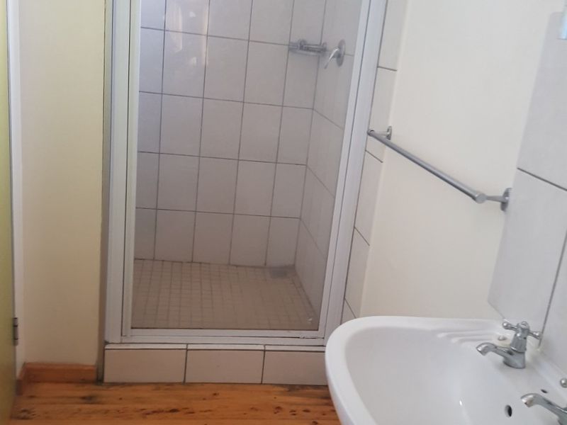 A functional bathroom featuring a shower enclosure, pedestal basin, and timber flooring, providing a clean and practical space.