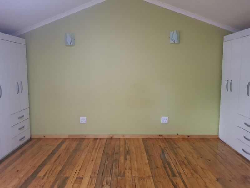 A bedroom featuring polished timber flooring, built-in wardrobes on either side, and wall-mounted lighting.