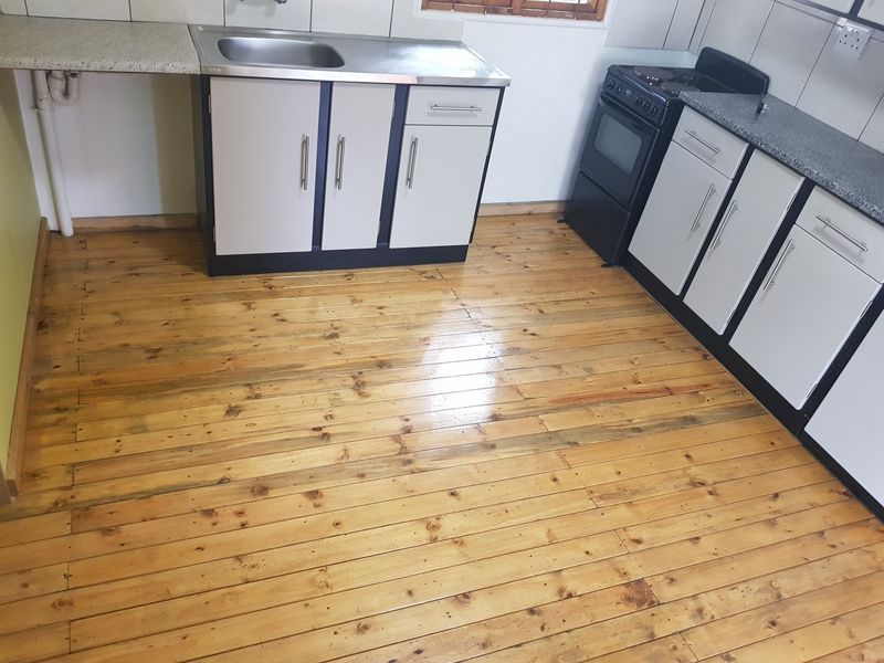 A functional kitchen featuring timber flooring, built-in cabinetry, a stainless steel sink, and a freestanding stove with tiled splashback.