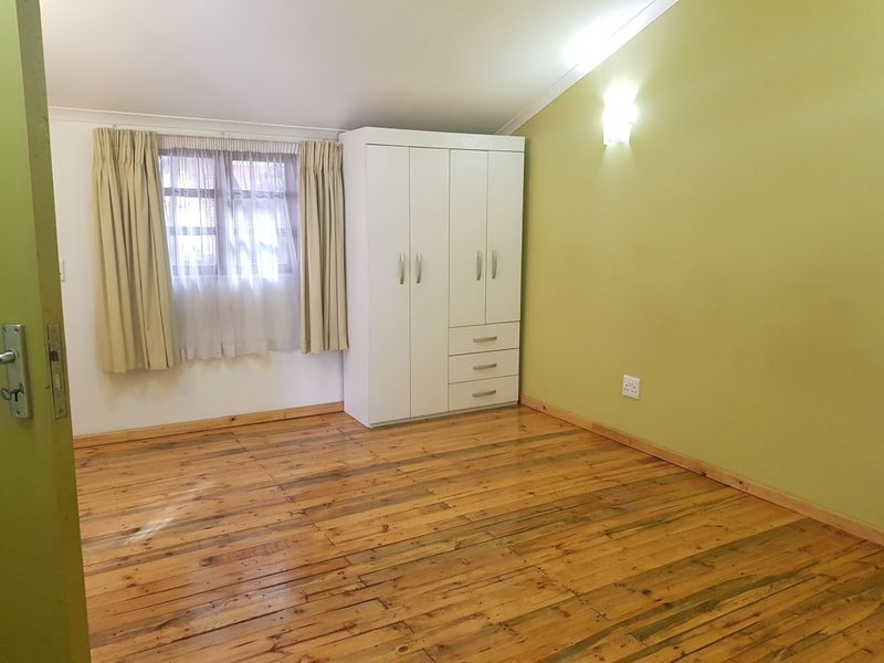 A bedroom featuring natural timber flooring, a built-in wardrobe, and a sloped ceiling with a wall-mounted light fixture.