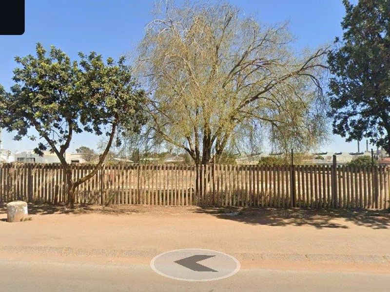 Street view of the commercial property frontage featuring a wooden picket fence and mature trees along the unpaved verge.