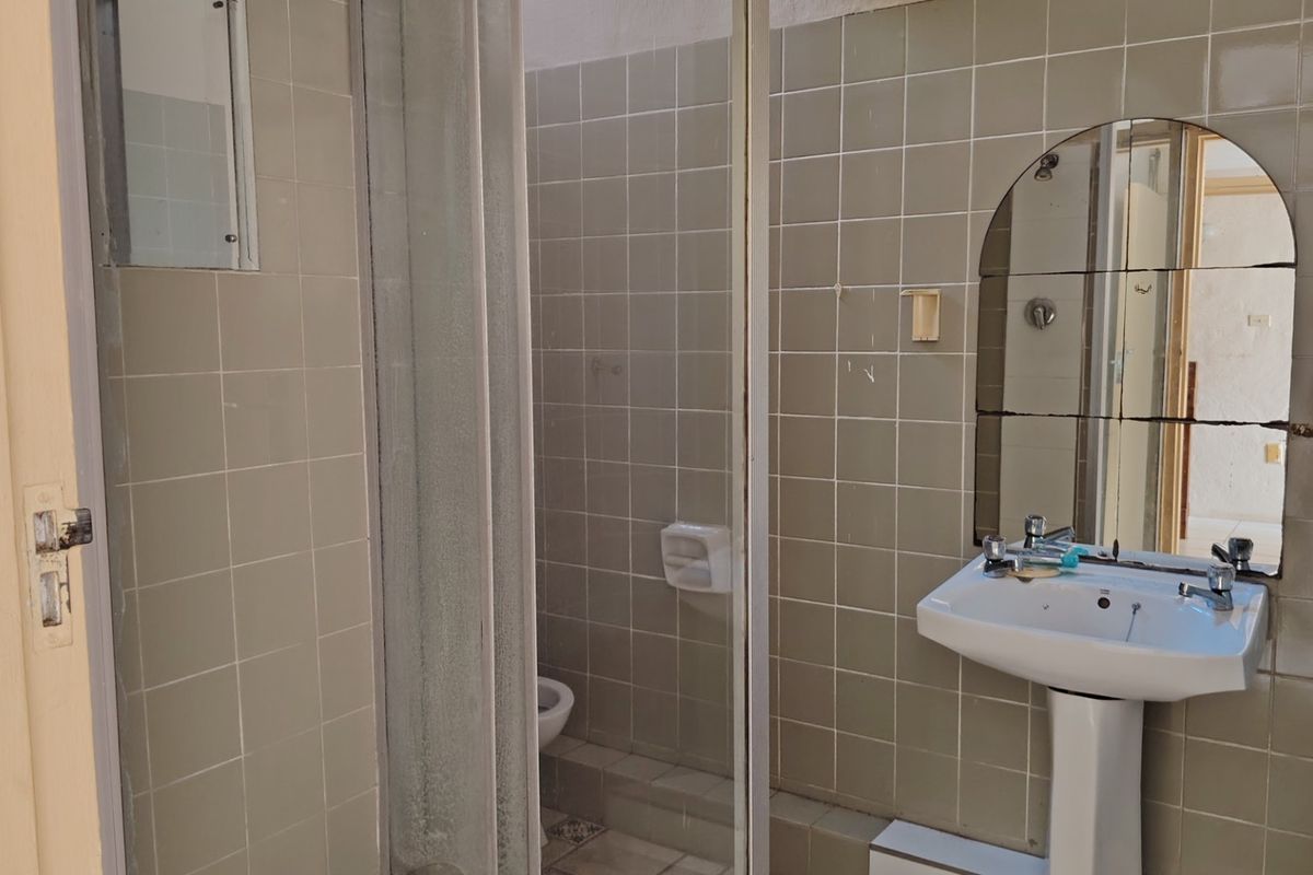 A dated bathroom featuring a pedestal basin, tiled walls, and a shower enclosure, requiring modernization to improve its aesthetic and functionality.
