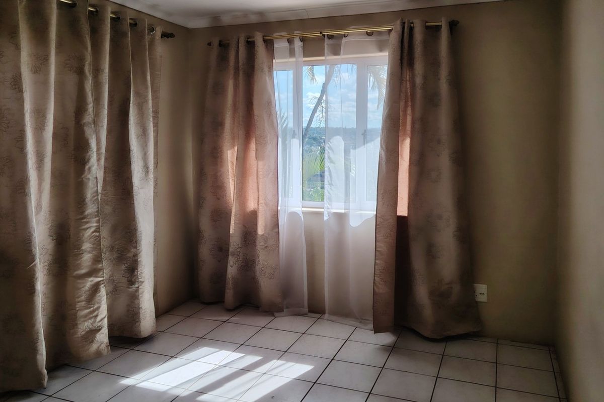 A bright, empty bedroom featuring neutral tiled flooring and large windows with curtain rods, offering a blank canvas for personalization.