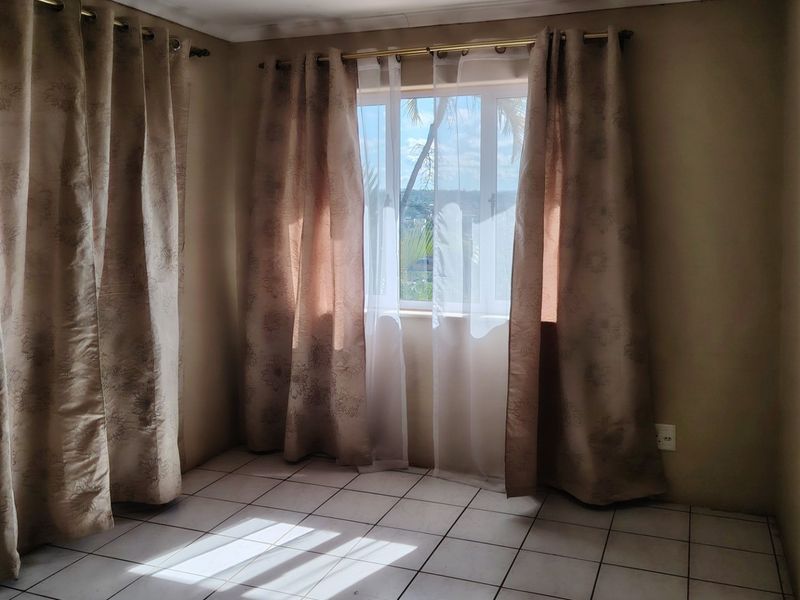 A bright, empty bedroom featuring neutral tiled flooring and large windows with curtain rods, offering a blank canvas for personalization.