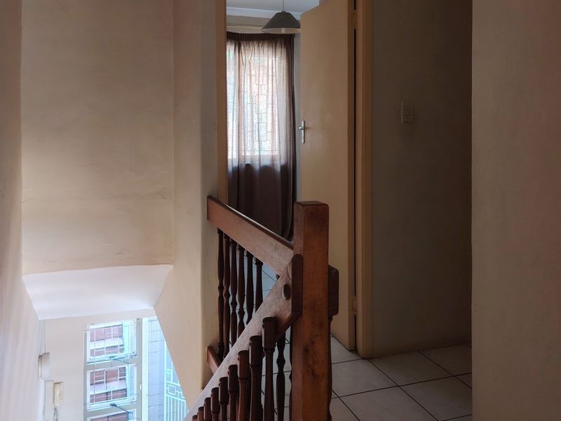 A functional hallway featuring a wooden balustrade staircase and tiled flooring, providing access to adjacent rooms.