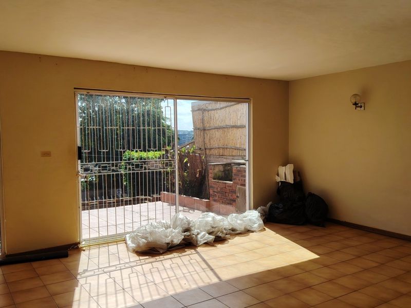 An empty living room featuring tiled flooring and a large sliding glass door with a security gate, providing access to an outdoor area.