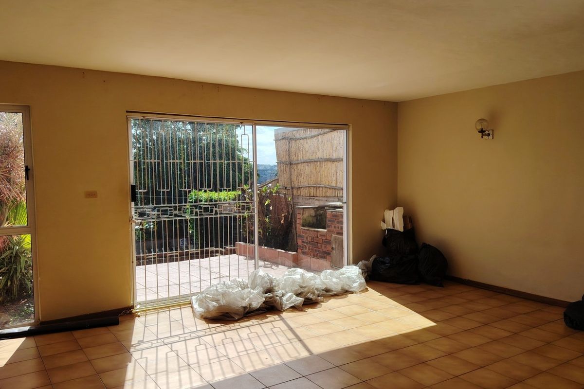An empty living room featuring tiled flooring and a large sliding glass door with a security gate, providing access to an outdoor area.