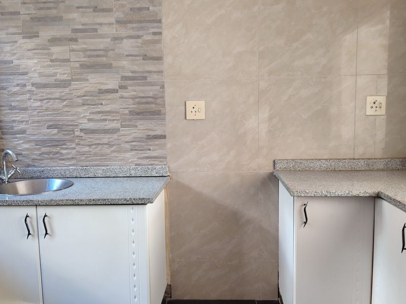 A clean, modern kitchen area featuring granite countertops, white cabinetry, and a stainless steel sink with a tiled splashback.