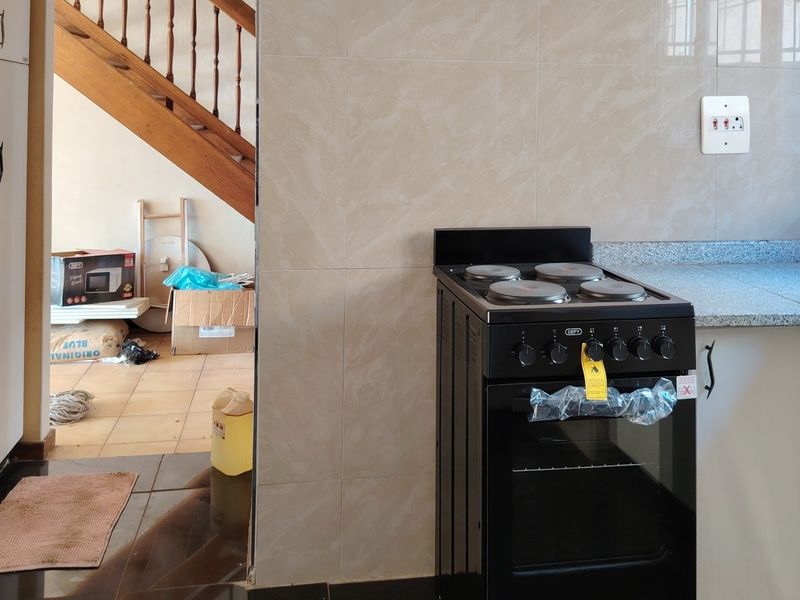 A kitchen area featuring a freestanding electric stove, granite countertops, and tiled splashbacks, with an adjacent view of a staircase and hallway.