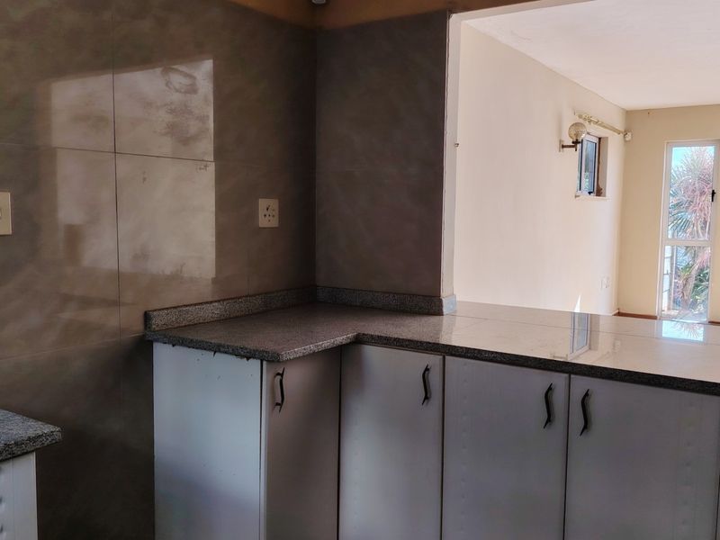 A functional kitchen area featuring granite countertops, built-in cabinetry, and a tiled backsplash, with an open-plan layout connecting to the adjacent living space.