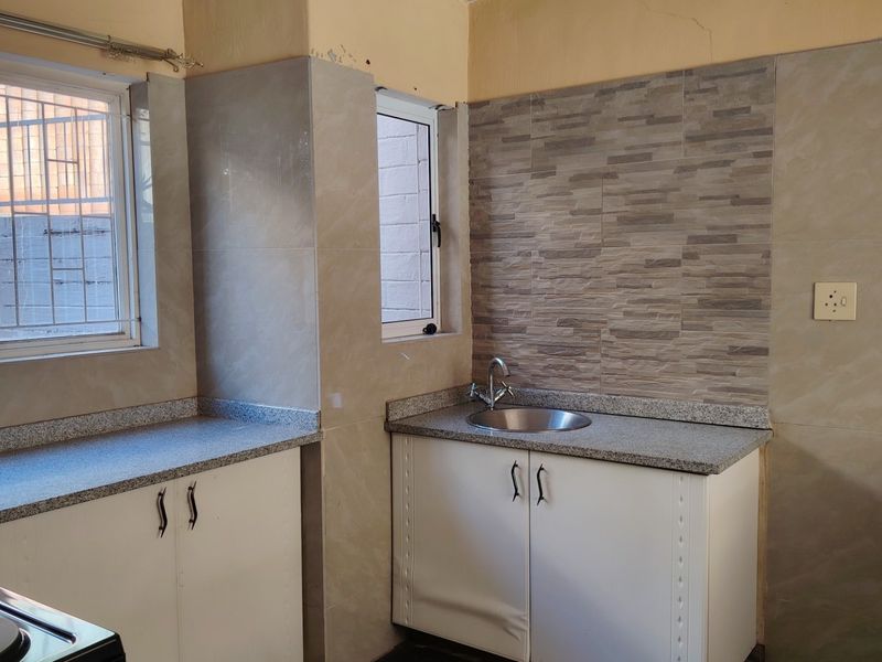 A compact kitchen area featuring granite countertops, a stainless steel sink, and tiled wall finishes, currently vacant and ready for updates.