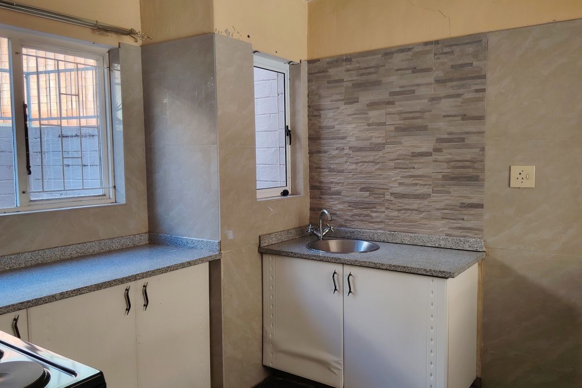 A compact kitchen area featuring granite countertops, a stainless steel sink, and tiled wall finishes, currently vacant and ready for updates.
